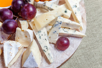 Board with different types of cheese: Dor blu, chedar, Parmesan, brie, honey sauce, finger bread and grape. Restaurant menu plate