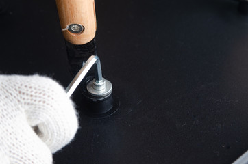 Close up of gloved hand tightening screw with allen wrench on black furniture surface showcasing DIY assembly and repair work