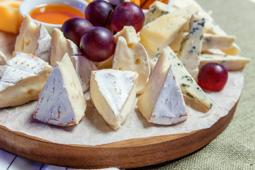 Board with different types of cheese: Dor blu, chedar, Parmesan, brie, honey sauce, finger bread and grape. Restaurant menu plate