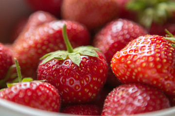 ripe strawberry berry with green leafs in a plate on a green background