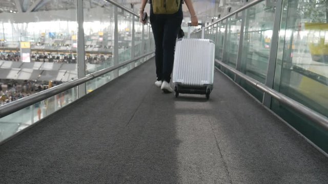 Close up of woman walking with trolley suitcase at airport. People and lifestyles concept. Back view and low angle