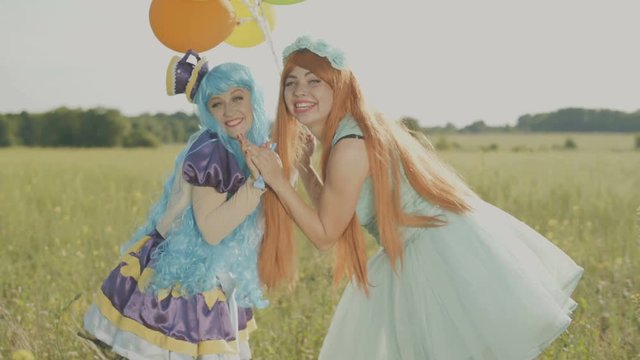 Two cheerful girls in bright costumes of princesses and with balloons are having fun in the field.