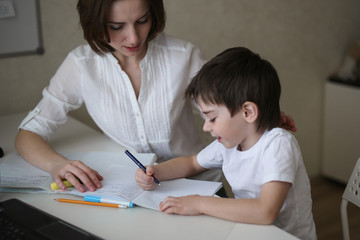 beautiful mother teaches her son at home at table
