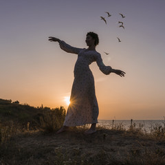 Adorable Caucasian Brunette girl in Light Dress Enjoying at the Seacoast at Sunrise time.