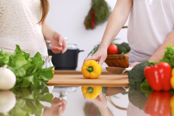 Closeup of human hands cooking in kitchen. Mother and daughter or two female friends cutting vegetables for fresh salad. Healthy meal, vegetarian food and lifestyle concepts
