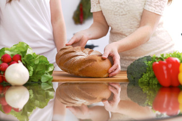 Closeup of human hands cooking in kitchen. Mother and daughter or two female friends cutting bread. Healthy meal, vegetarian food and lifestyle concept