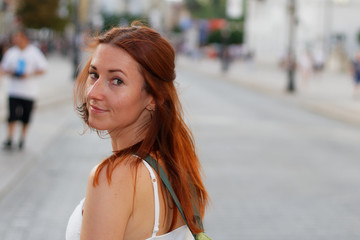 Young beautiful redhead woman looking back walking down a street