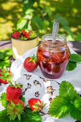 Strawberry jam and juicy ripe strawberries on a wooden table in the garden on a summer sunny afternoon in a rustic style, the concept of gardening, healthy organic vitamin nutrition