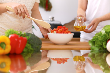 Closeup of human hands cooking in kitchen. Mother and daughter or two female friends cutting vegetables for fresh salad. Healthy meal, vegetarian food and lifestyle concepts