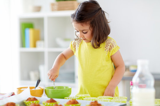 family, cooking, baking and people concept - little girl making batter for muffins or cupcakes at home kitchen