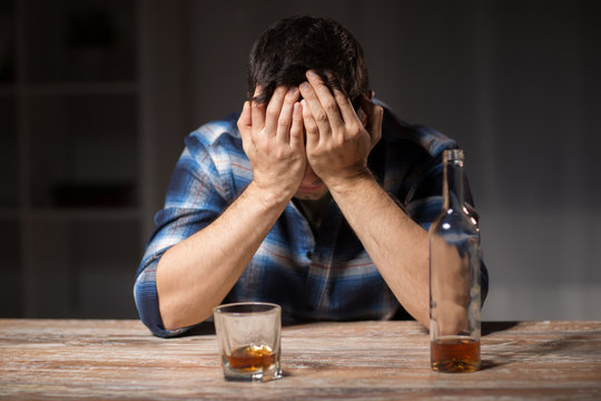 alcoholism, alcohol addiction and people concept - male alcoholic with bottle and glass drinking whiskey at night