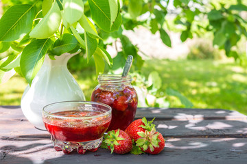Strawberry jam and juicy ripe strawberries on a wooden table in the garden on a summer sunny afternoon in a rustic style, the concept of gardening, healthy organic vitamin nutrition