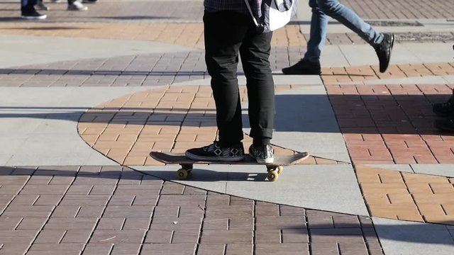 Boy legs riding a skateboard on a pedestrian street pavement slow motion
