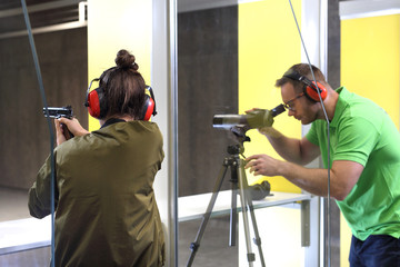 Nauka strzelania. Kobieta strzela z broni na strzelnicy pod okiem instruktora. - obrazy, fototapety, plakaty