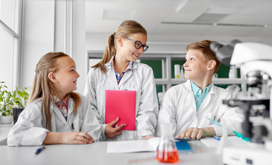 education, science and children concept - happy kids with workbooks studying chemistry at school laboratory