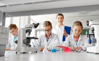 education, science and children concept - teacher and students studying chemistry at school laboratory and writing to workbooks