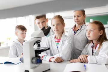 Fototapeta premium education, science and children concept - kids or students with microscope studying biology at school laboratory