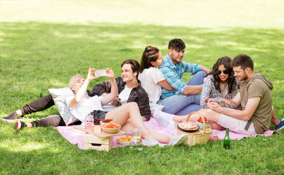 friendship, leisure, technology and people concept - group of friends with smartphones and non alcoholic beer chilling on picnic blanket at summer park