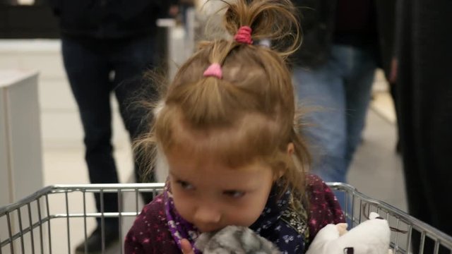 Family shopping - child girl sits in the commodity trolley in a huge mall