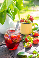 Strawberry jam and juicy ripe strawberries on a wooden table in the garden on a summer sunny afternoon in a rustic style, the concept of gardening, healthy organic vitamin nutrition