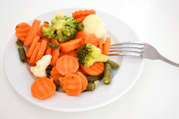 Vegetables cooked on steam. Vegetarian dish. Cauliflower, broccoli, asparagus and carrots on a white plate and against a white background. Vitamin salad for a diet.