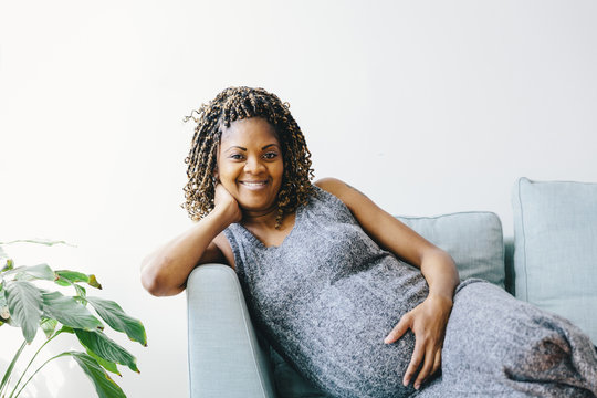 Portrait of pregnant woman leaning on sofa against wall at home