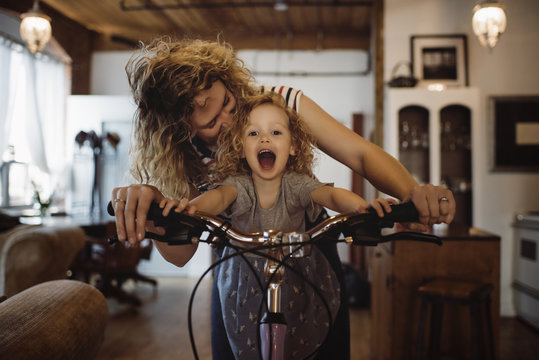 Cheerful mother with daughter riding bicycle at home