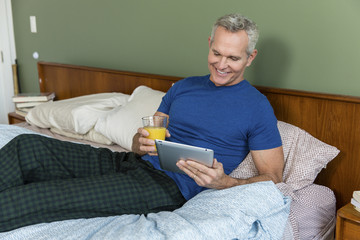 Senior man holding juice while using tablet computer on bed at home