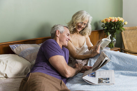 Smiling woman showing book to man while sitting on bed at home