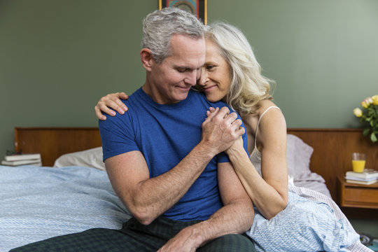 Loving man holding woman's hand while sitting on bed at home