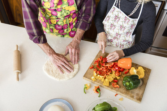 Midsection of woman cutting bell pepper while man making pizza dough in kitchen at home