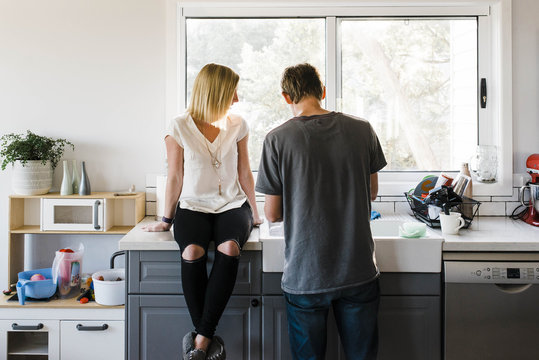 Woman Sitting On Kitchen Counter By Man At Home