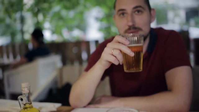 A young man sitting with a friend in a pizzeria drinking beer clinking glasses. Communication after a working day
