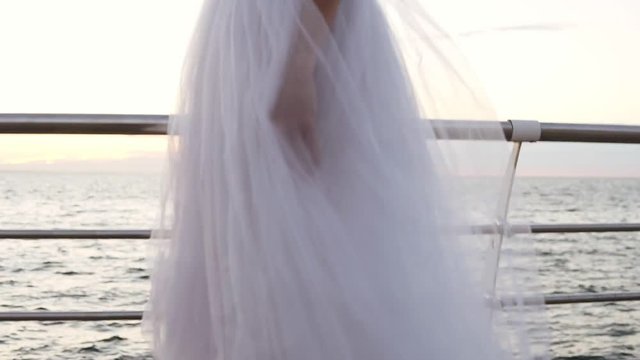 Close up footage of graceful ballerina in white long tutu and pointe walking tiptoe on wooden floor ner the sea or ocean. Daytime