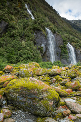 Red glacial rocks in front of waterfalls at Franz Josef Glacier, New Zealand