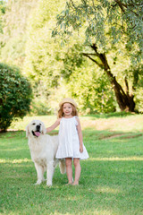 A cute blonde girl with blue eyes and a white big dog in a summer sunny park. The concept of friendship.