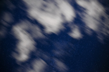 Background of dark-blue night sky with countless twinkle stars and moving white clouds upon on it