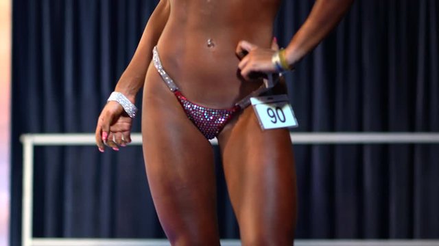 Muscular yong woman in bikini posing in bodybuilding championship. Sport competition, lifestyle and people concept.