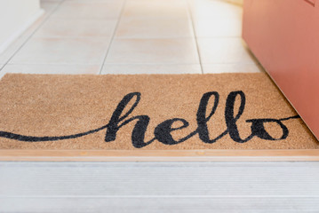 Open door with a natural fiber rug with the word hello written in script © Kristen