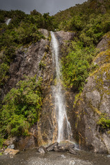 Waterfall creating a small rainbow and vegetation on a stormy day at Franz Josef Glacier, south island New Zealand