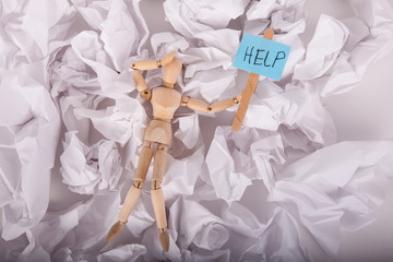 Manikin doll frustrated holding a help sign laying on crumbled sheets of paper 