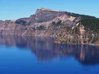Fototapeta na wymiar The magnificent rich blue waters of Crater Lake with reflections of the rim in the forests of Southern Oregon on a beautiful sunny summer morning. 