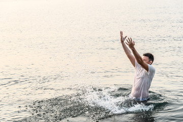 A young man standing on the waist in the sea created a very high wall of splashes with the movement of his hands