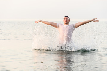 A young man jumps out of the water with his hands raised to the sides