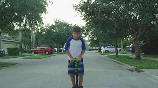 Slow motion of boy bouncing on a pogo stick while smiling and looking at camera
