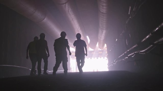 silhouette of many construction workers walking out from a large tunnel