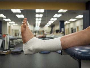 Athlete's foot with an ankle tape job for support hanging off a table in a medical clinic  - obrazy, fototapety, plakaty