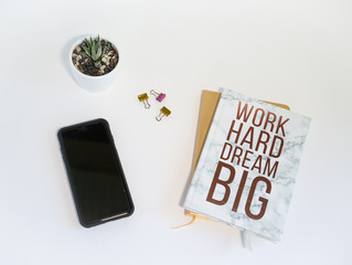 White overhead desktop with cell phone, plant and books with motivational message 