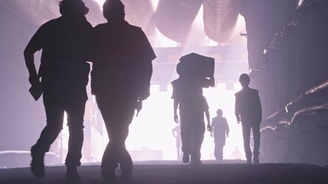 silhouette of many construction workers walking out from a large tunnel