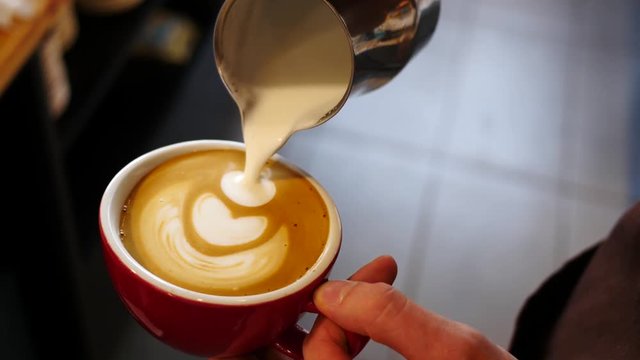 Barista draws milk over a coffee - making latte art for cappuccino